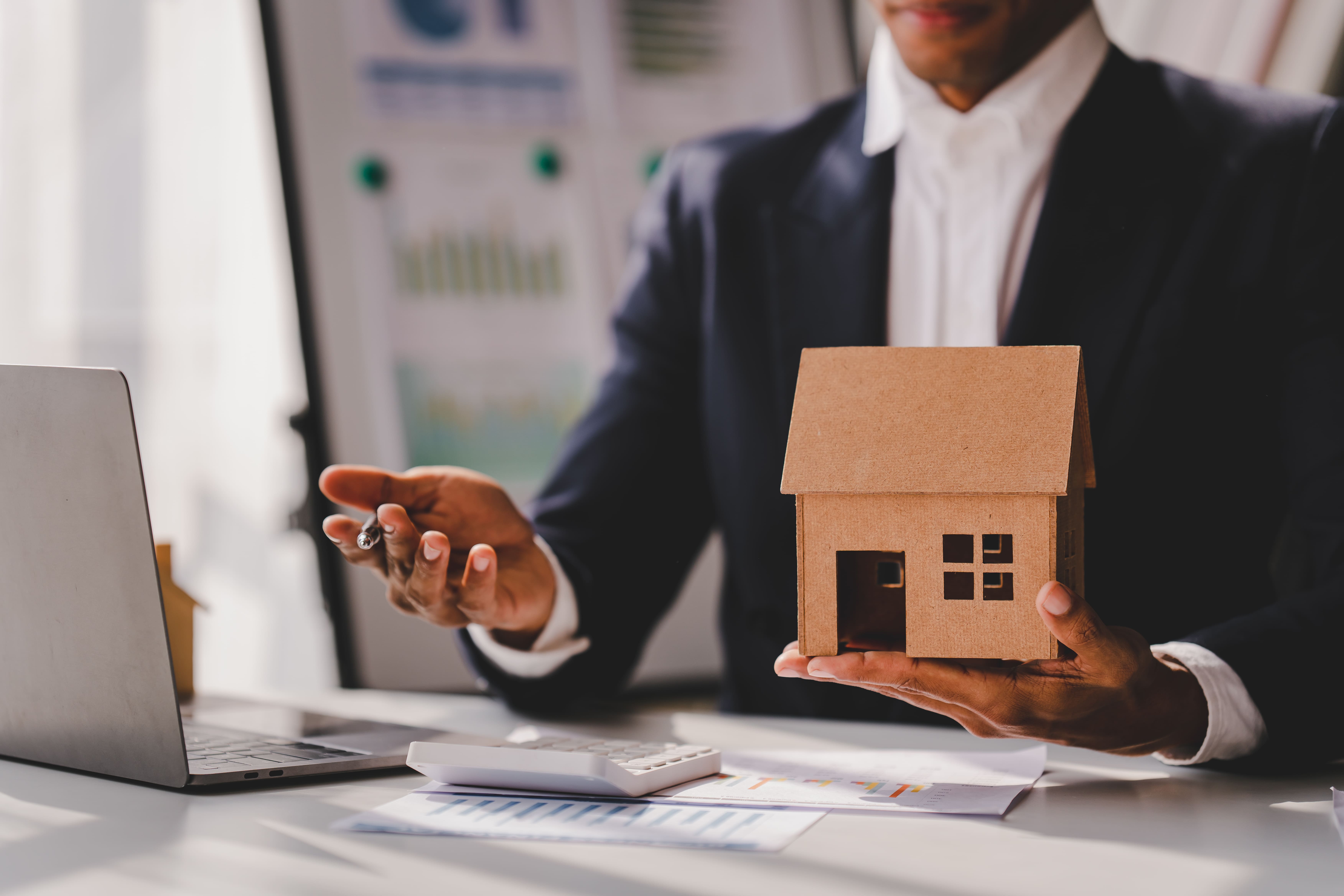 Agent holding a cardboard house model while presenting an investment deal