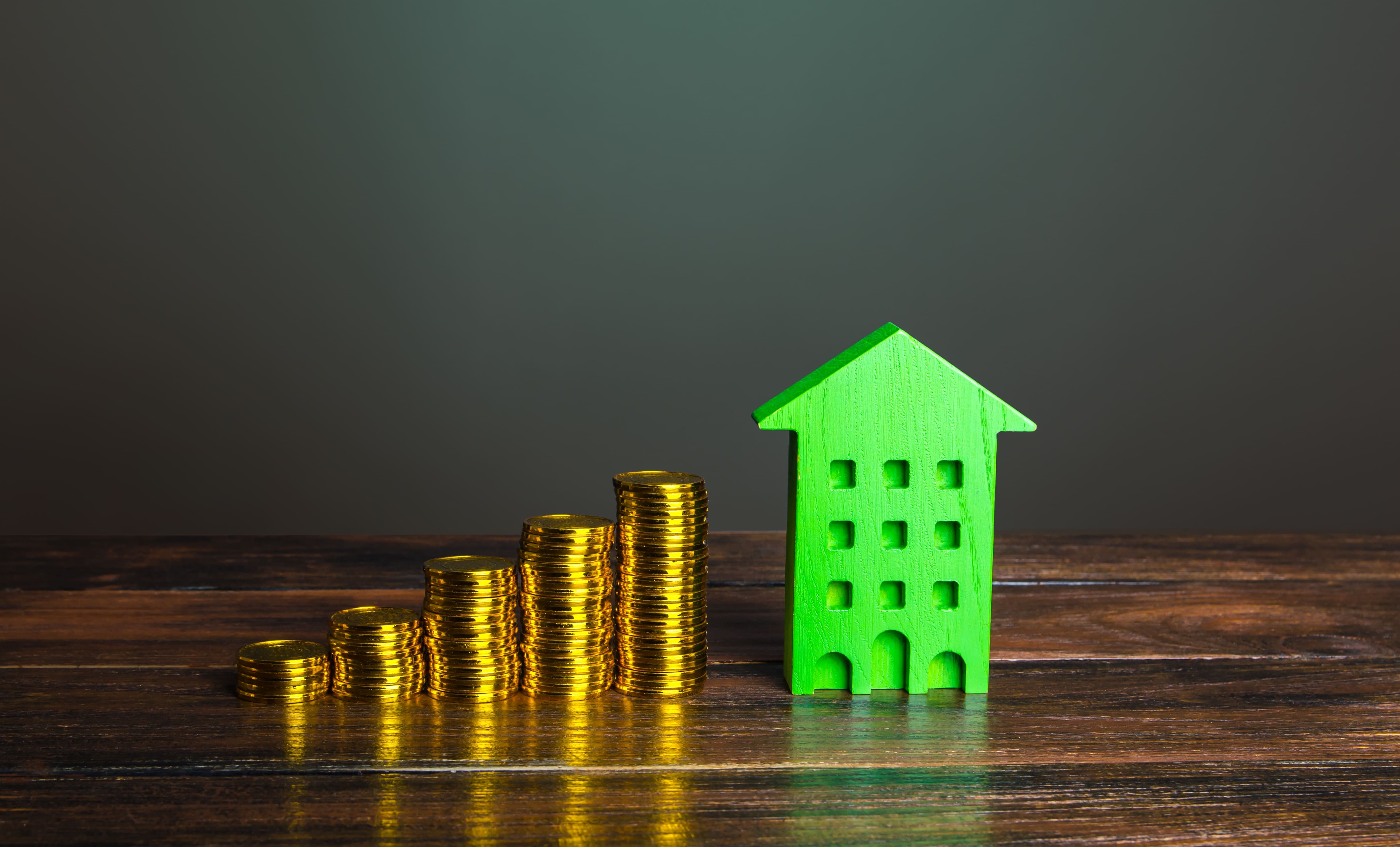 Coins beside a green property model representing real estate capital growth