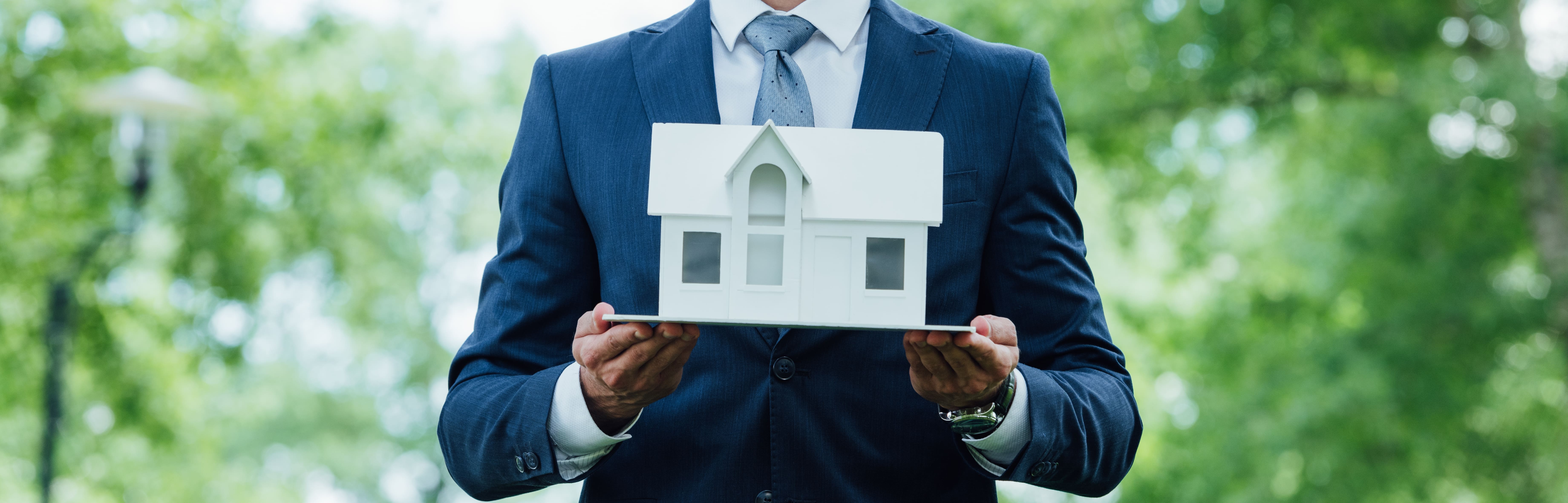 Professional holding a white house model outdoors representing property ownership