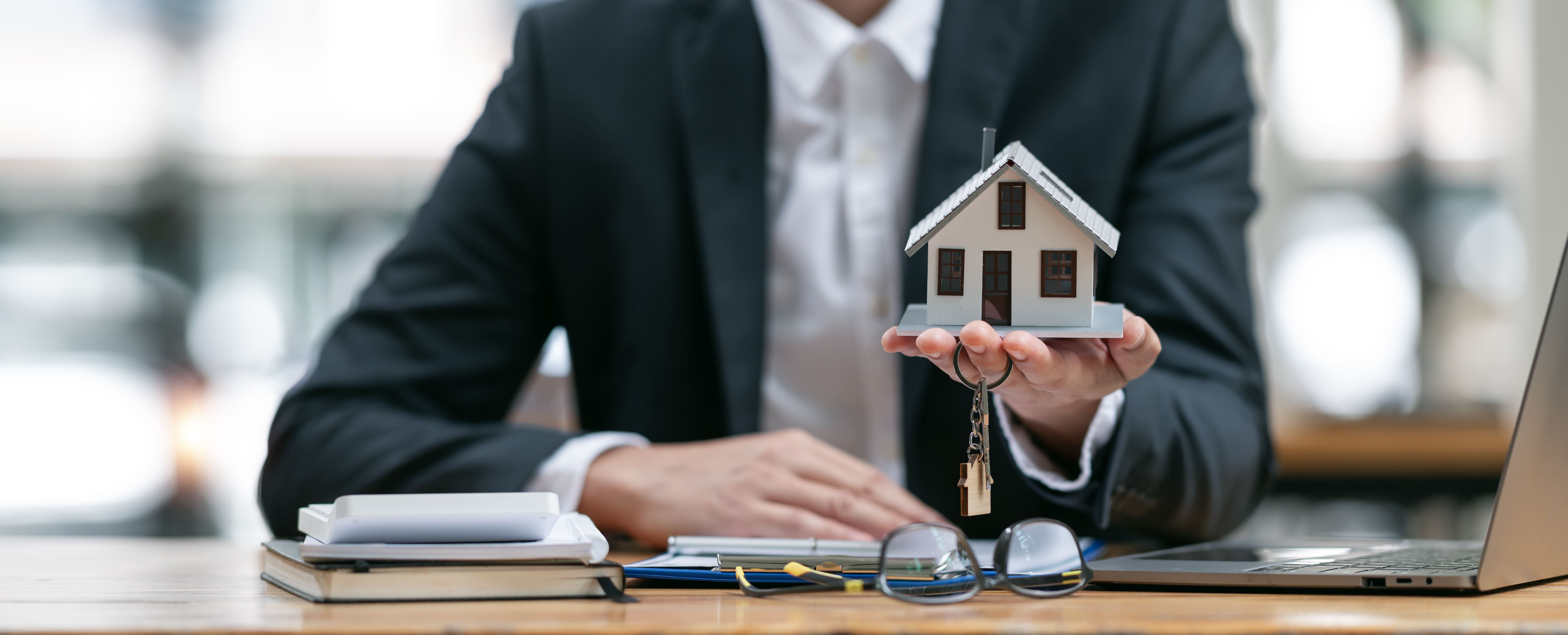 Agent presenting a house model and property keys across a desk to a client