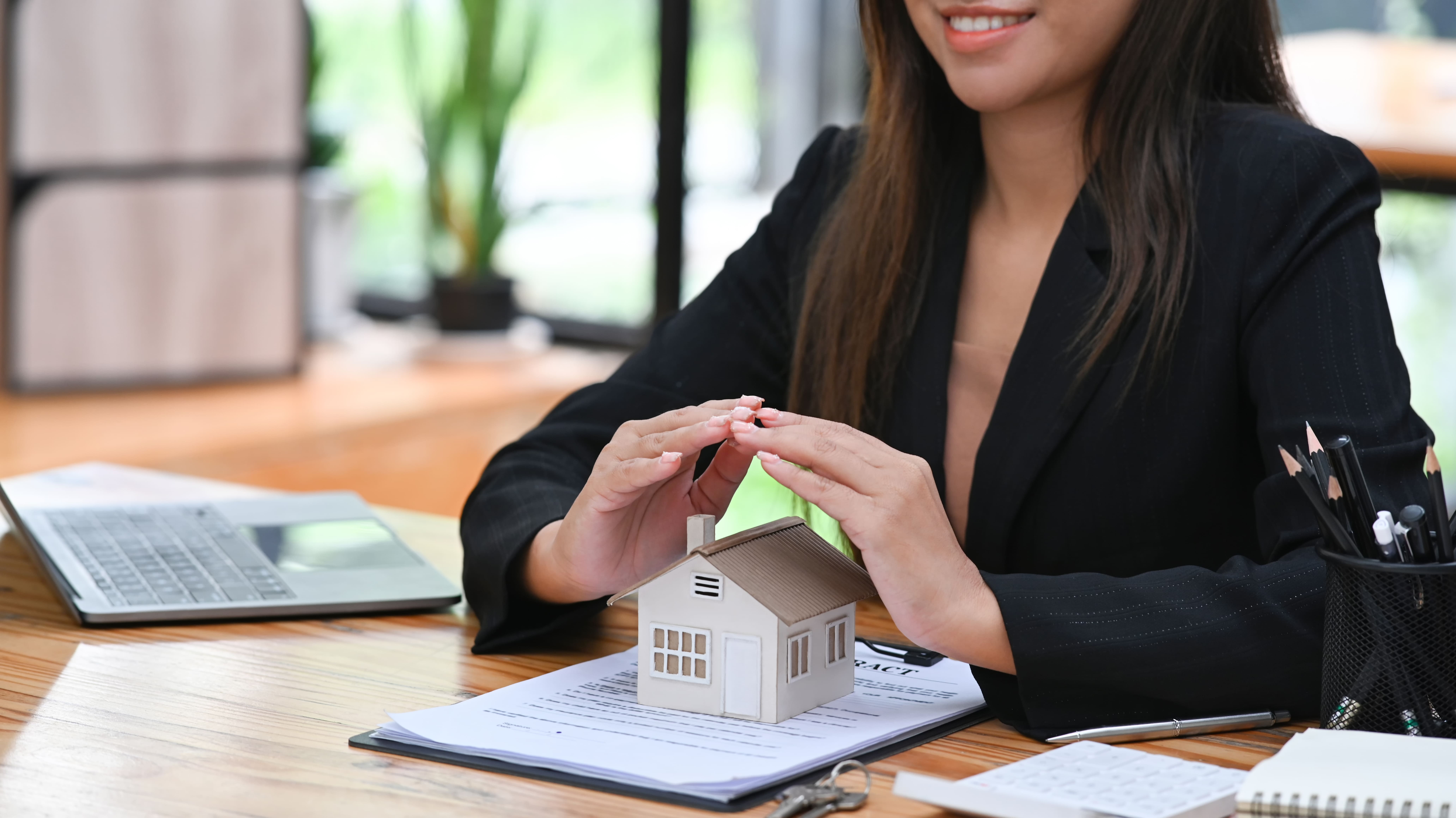 Agent placing hands over a property model on top of a contract document