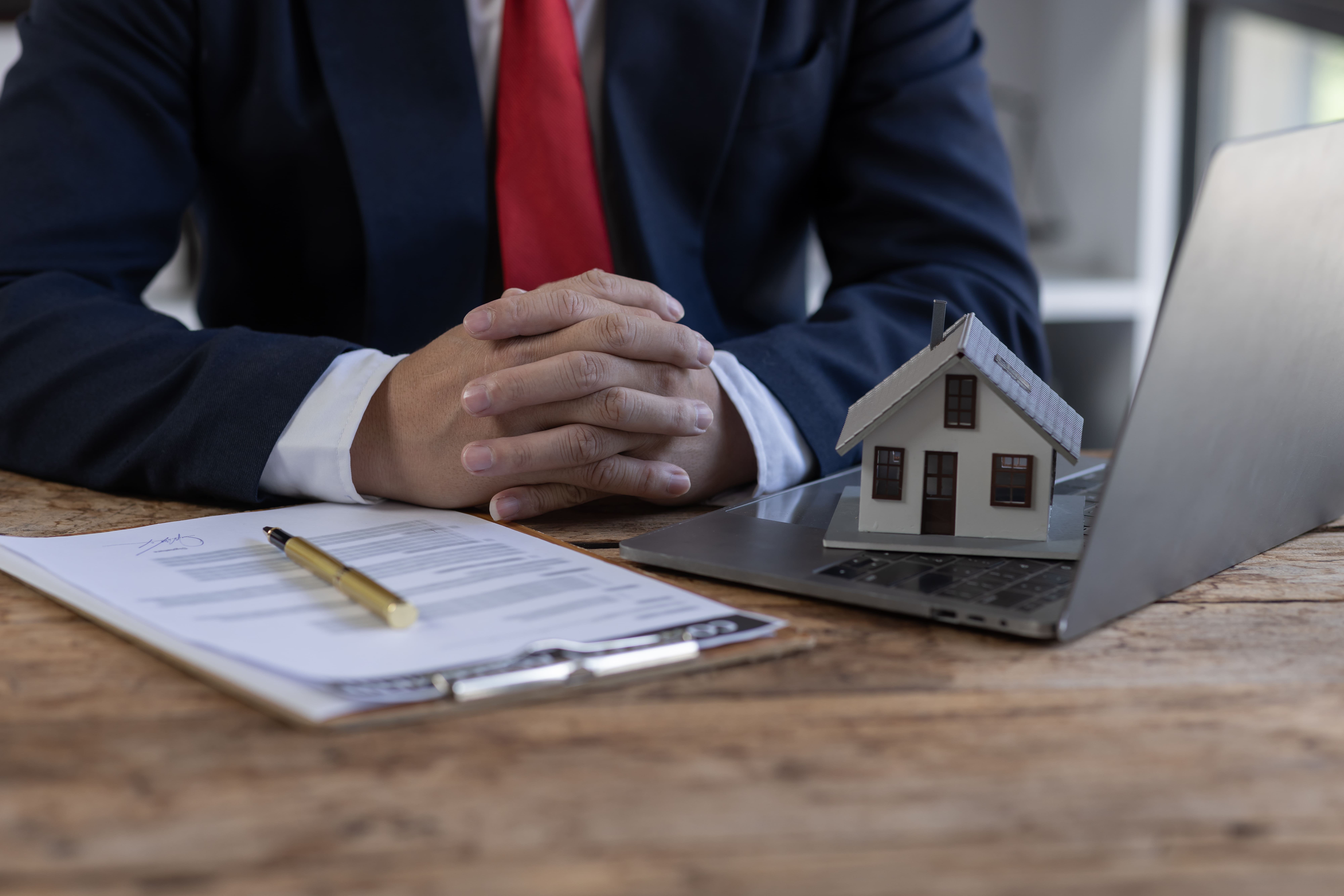 Senior broker at a desk reviewing a house model and contract documents
