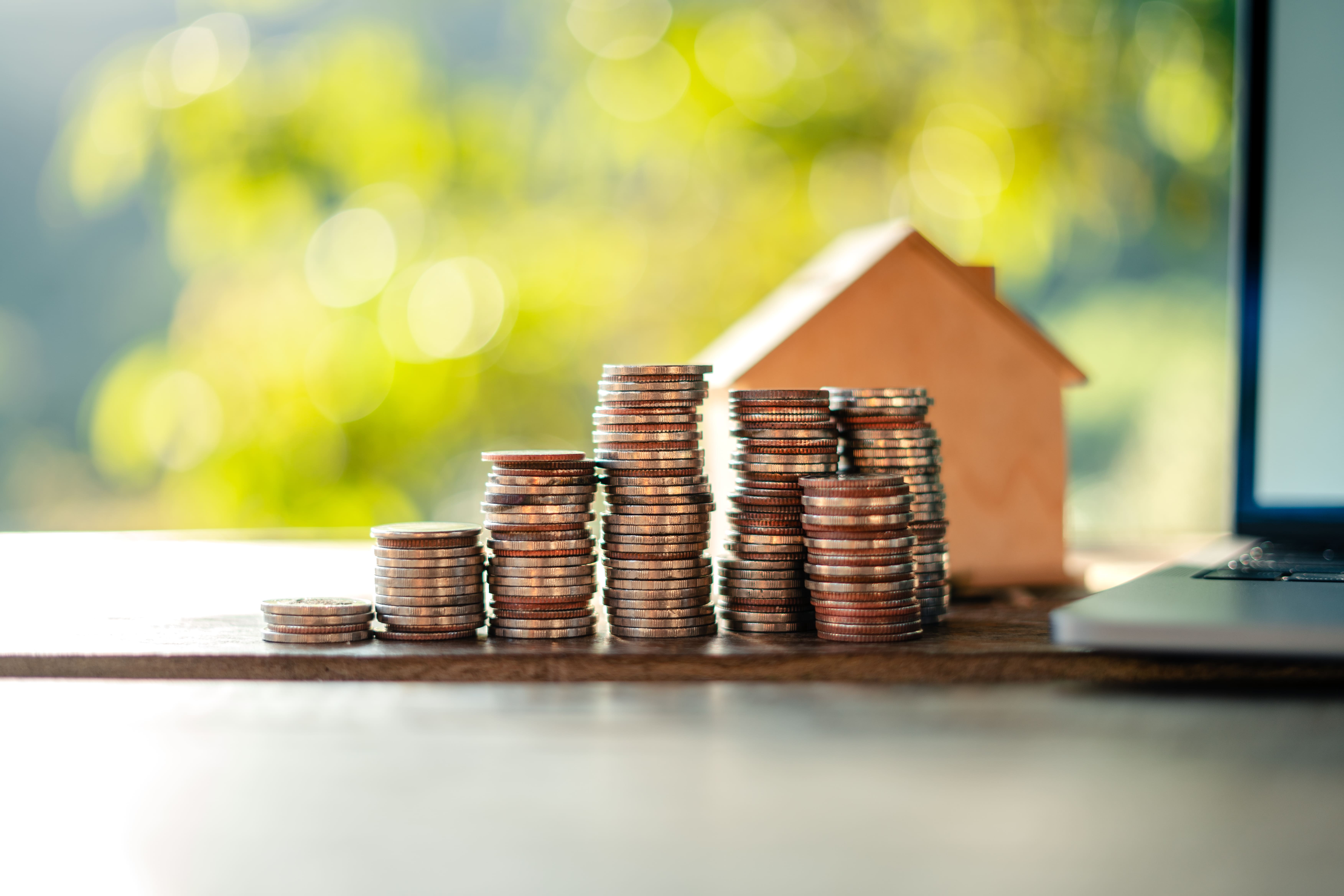 Growing coin stacks beside a house model and open laptop