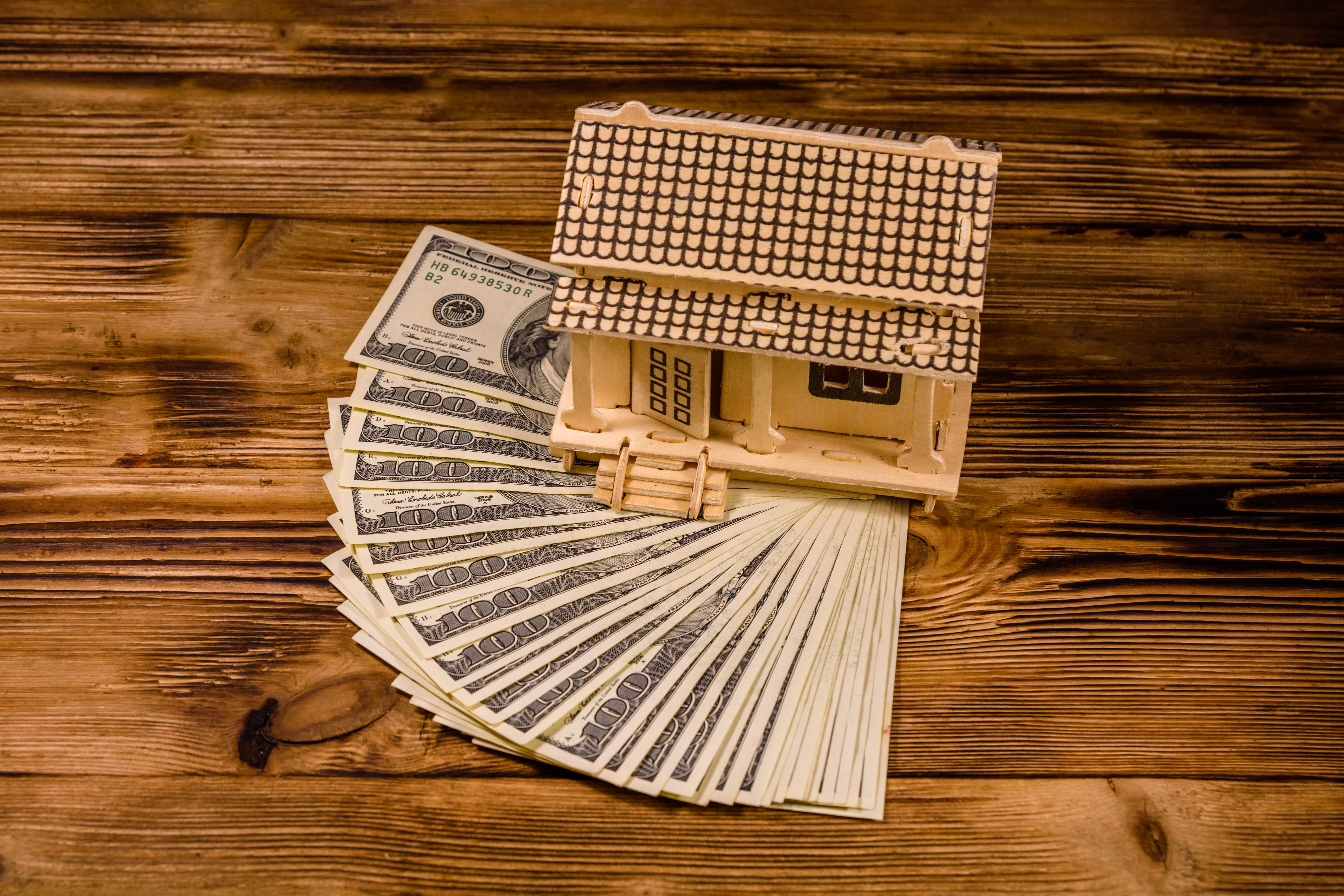 Wooden house model placed on a fan of cash banknotes