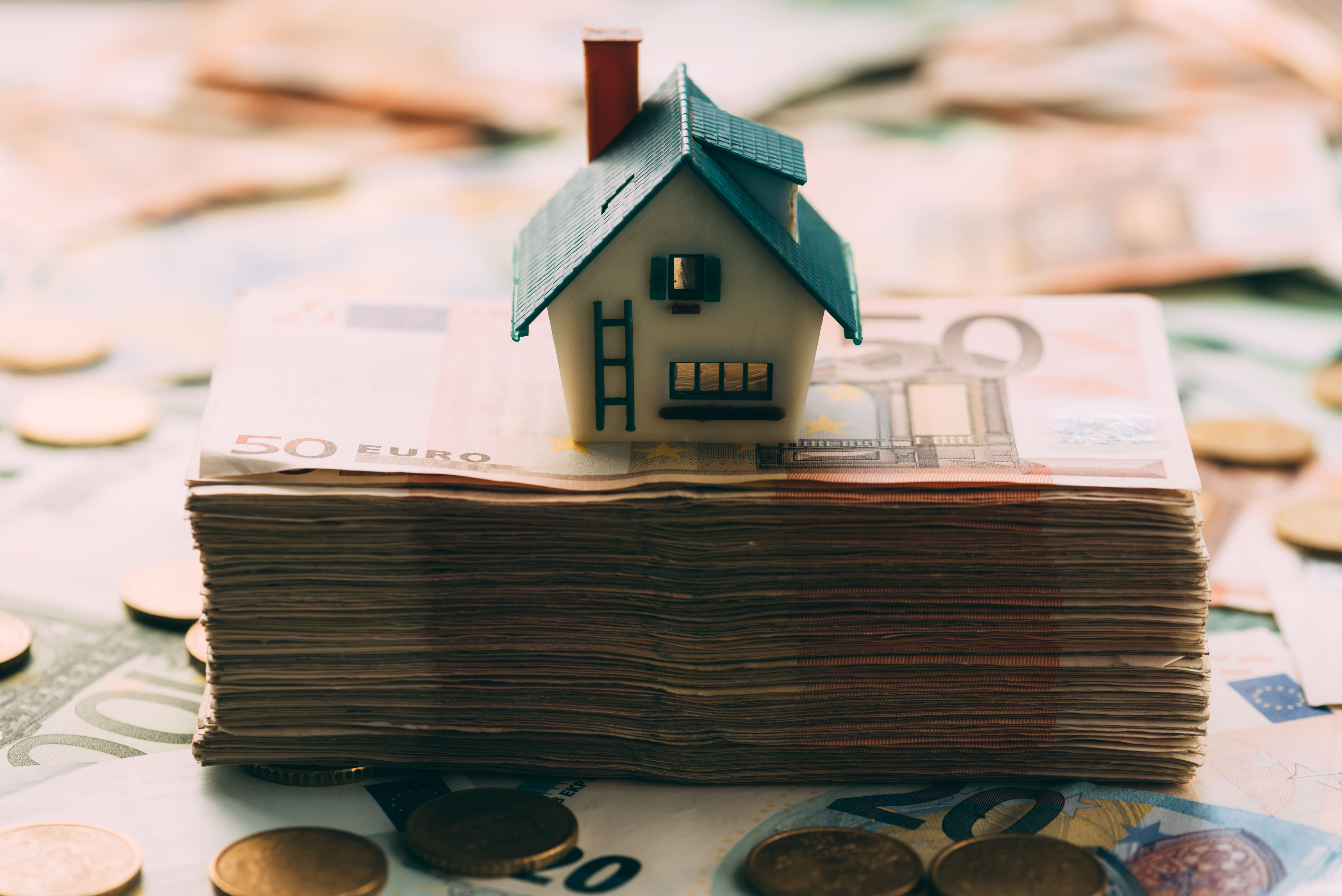 House model on stacked banknotes representing real estate investment value
