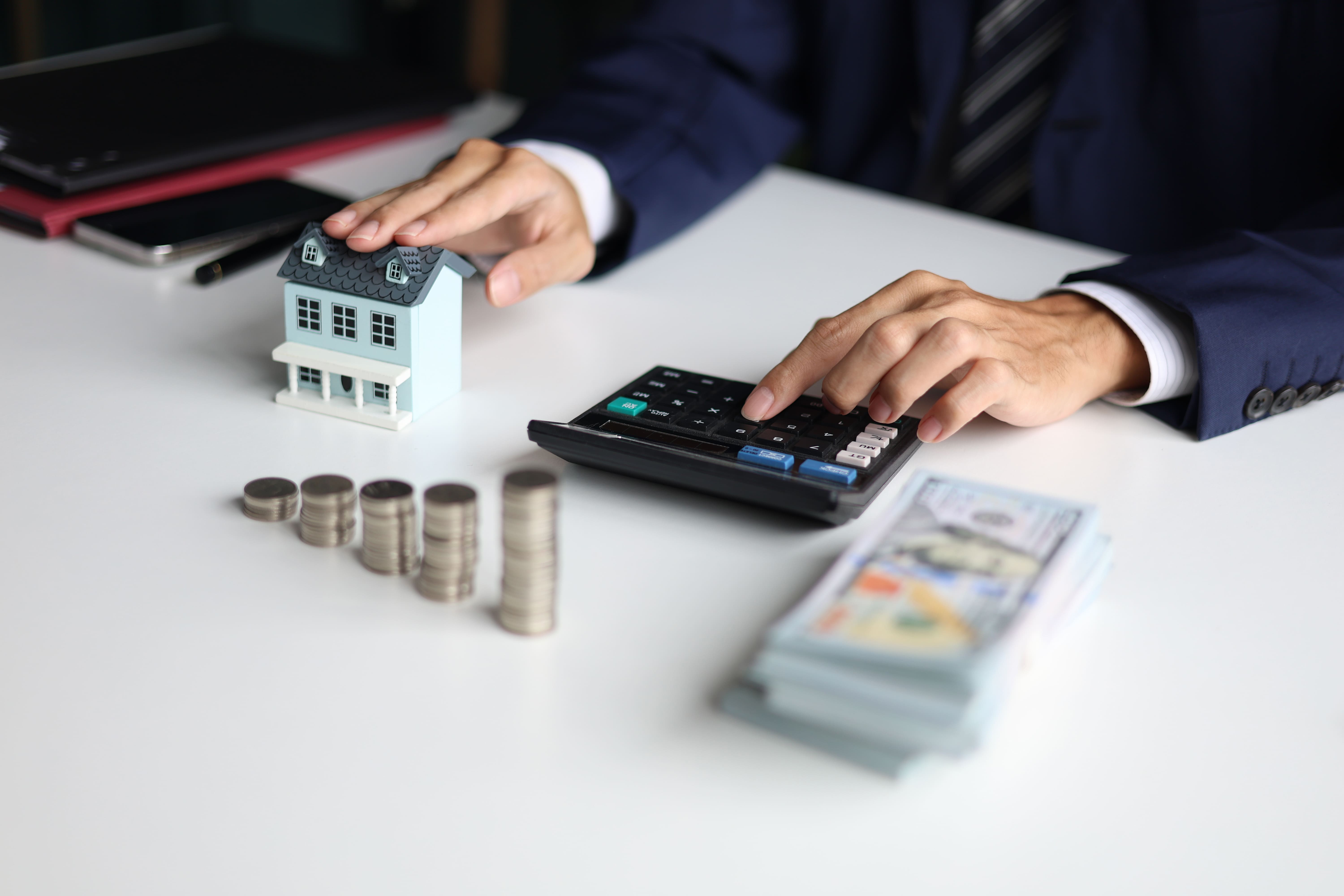 Investor calculating returns with a house model, coins, and cash