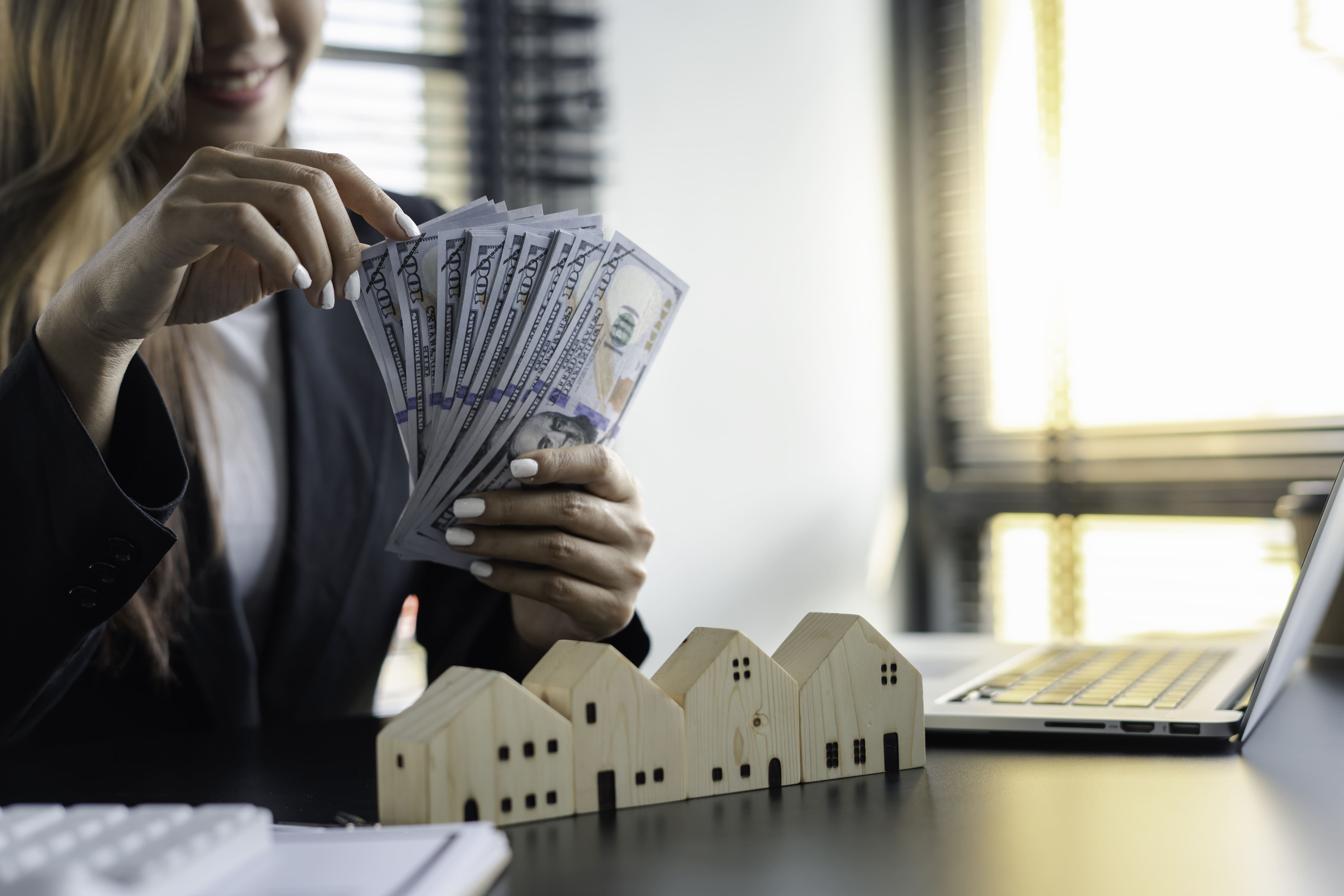 Female investor counting cash alongside property portfolio models
