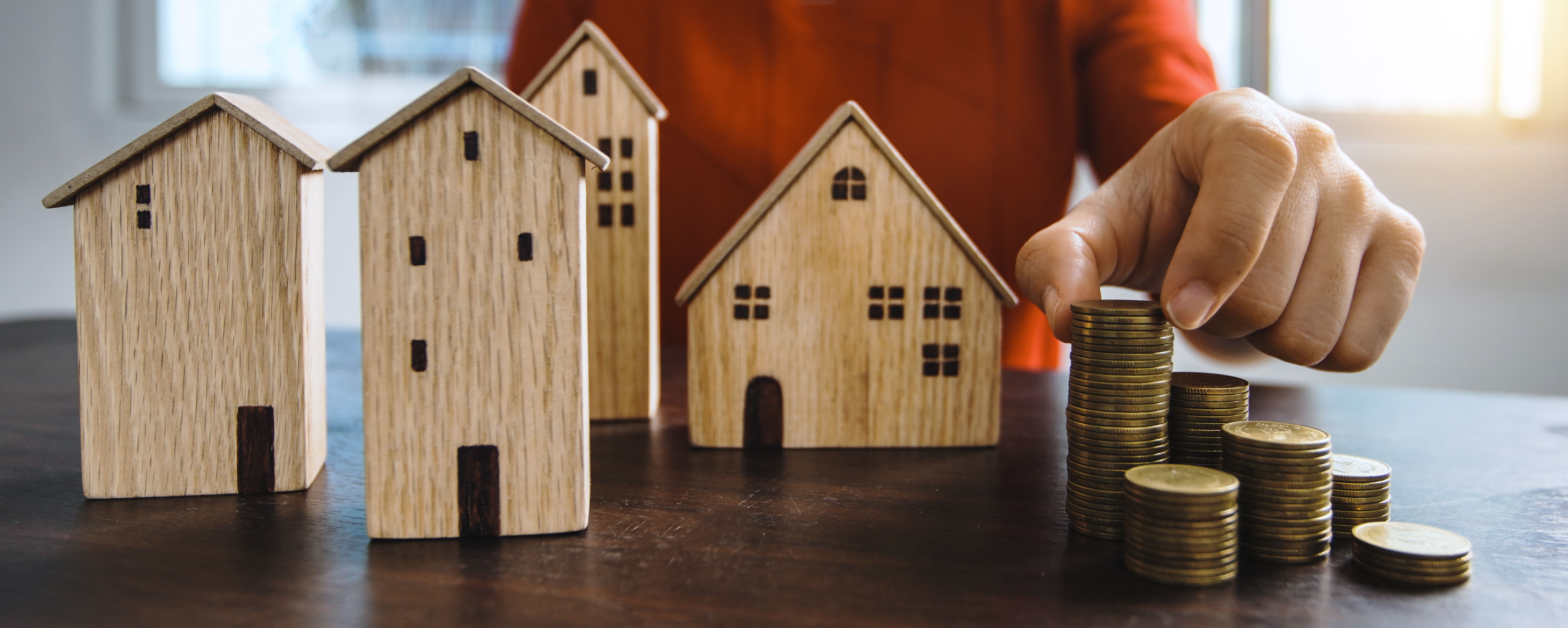 Wooden houses beside stacked coins representing portfolio building