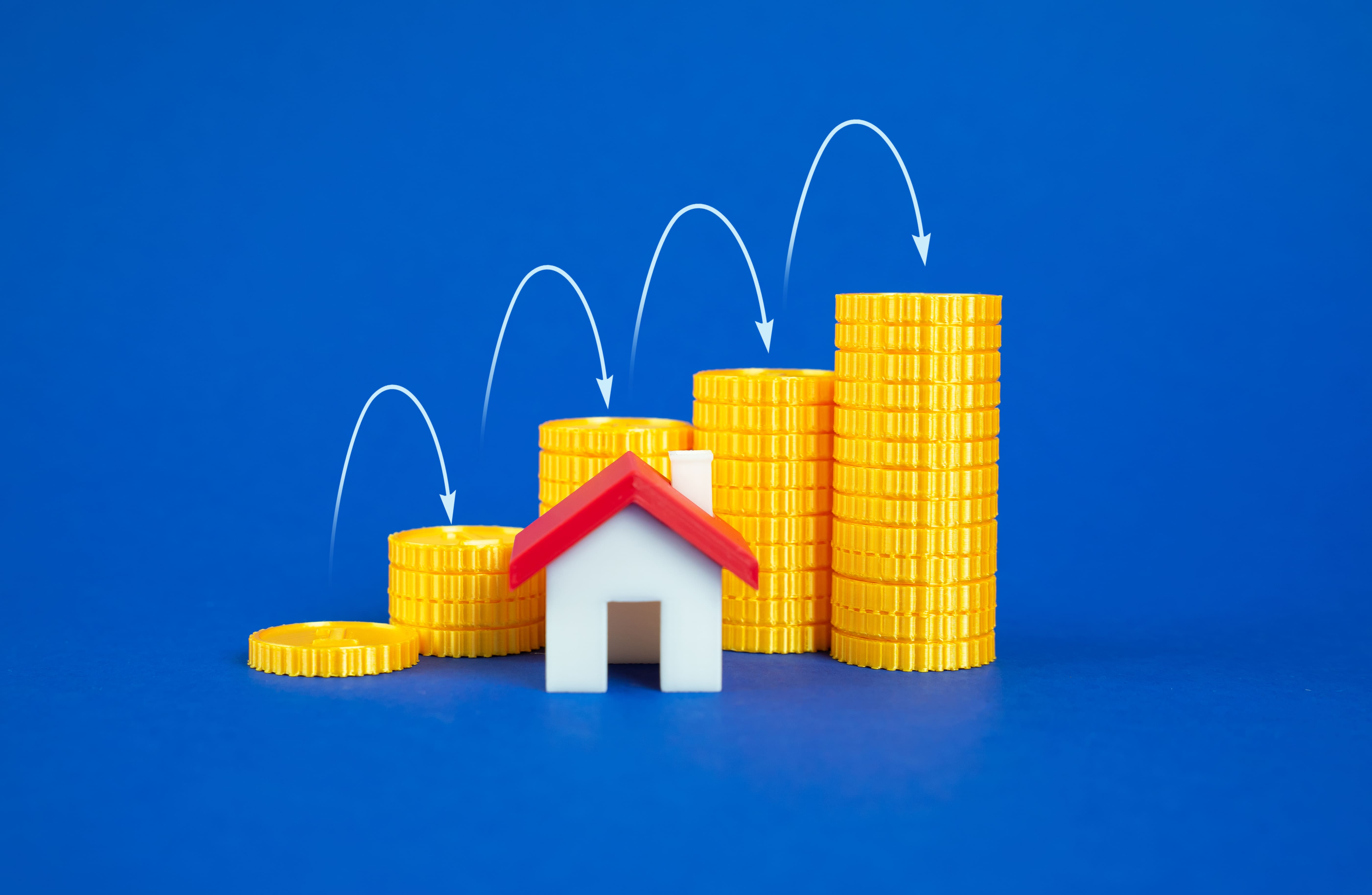Growing coin stacks beside a house model representing real estate ROI